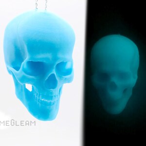 May include: A light blue glow-in-the-dark skull pendant necklace. The skull is made of plastic and has a smooth, rounded surface. The necklace is hanging from a silver chain.
