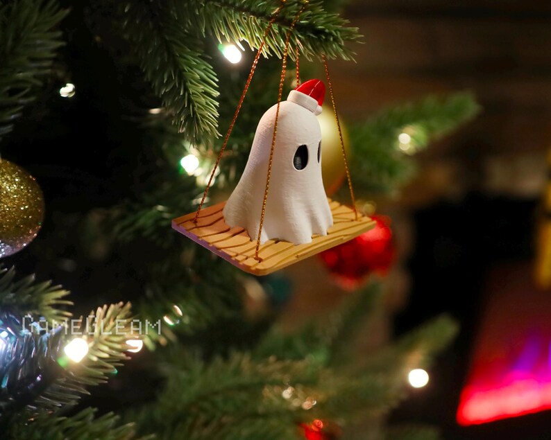 A top down view of a white Santa ghost on a brown swing ornament hanging on a holiday Christmas tree with lights in the background.