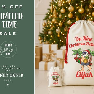 May include: Two white Christmas gift bags with red drawstrings. The larger bag features the text "Da Kine Christmas Delivery" and a cartoon Santa Claus with sunglasses, a surfboard, and a pineapple. The name "Elijah" is printed below. A smaller matching bag is also present.