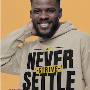 May include: A tan hoodie with the text "Just Never Strive Settle For Greatness" in black. The hoodie is worn by a smiling person with a dark beard and short hair. The background is a solid orange color.