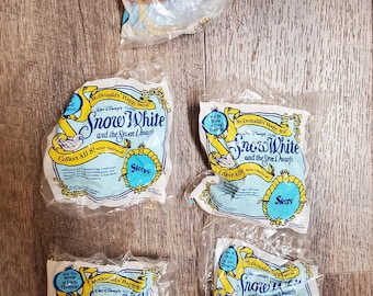 May include: Four plastic bags with the McDonald's Happy Meal logo and the Disney classic Snow White and the Seven Dwarfs. Each bag features a different dwarf, Sleepy, with a blue background. The bags are on a wood surface.