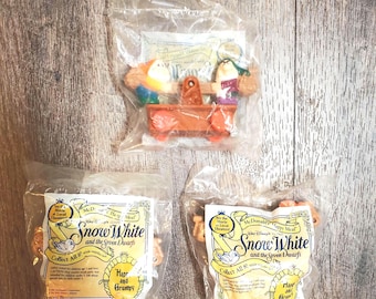 May include: Three McDonald's Happy Meal toys from Snow White and the Seven Dwarfs in clear plastic packaging. One package contains a brown seesaw with Happy and Grumpy figures. Two other packages feature printed labels with the movie title.