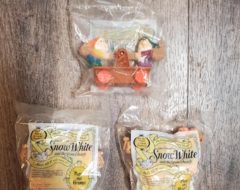 May include: Three plastic bags containing McDonald's Happy Meal toys from the Disney movie Snow White and the Seven Dwarfs. The toys are of the dwarfs, Happy and Grumpy. The bags are white with red and yellow text.