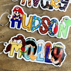 May include: Three colorful personalized keychains with names Avery, Hudson, and Molly. Each letter is decorated with different cartoon characters and patterns.