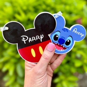 May include: Two character name tags, one featuring Mickey Mouse with the name "Parry" and the other featuring Stitch with the name "Avery".