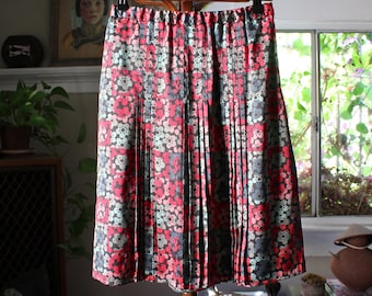Peut inclure: Jupe plissée à motifs floraux rouges, gris et bleu clair. La jupe est suspendue à un cintre en bois, mettant en valeur son design et sa texture. Le tissu semble léger, adapté aux températures plus chaudes. La jupe mesure environ 50 cm de long.