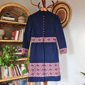 May include: A navy blue vintage dress with a mandarin collar and long sleeves. The dress has a red and white patterned band around the waist and hem.