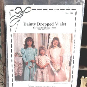 May include: A sewing pattern packet titled Dainty Dropped Waist Love and Stitches #154, featuring three children in dresses. The cover displays the text Sizes 4-14, 1995 Debbie Glenn, and Pattern Includes Smocking Plate and Alternate Front Panel Ideas.