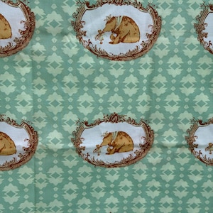 May include: A light green fabric featuring a repeating pattern of white oval frames with brown ornate borders. Inside each frame is a brown illustration of a bear wearing a crown and a small figure standing before it, set against a geometric background.