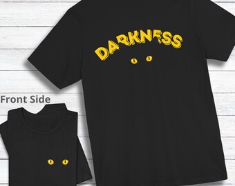 May include: Black t-shirt with the word "DARKNESS" in yellow outlined letters on the back. Two yellow eyes are below the word. The front of the shirt has two yellow eyes.