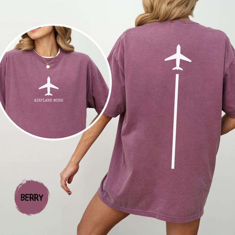 May include: Berry-colored t-shirt with a white airplane graphic and the words "AIRPLANE MODE" on the front. The back of the shirt features a white airplane graphic with a vertical line. The shirt is a comfortable, oversized fit.