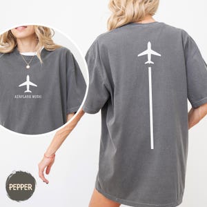 May include: Dark gray t-shirt with a white airplane graphic and the words "AIRPLANE MODE". The back of the shirt features a white airplane graphic with a white line extending downwards. The shirt is a comfortable, oversized fit.