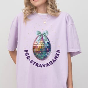May include: A lavender t-shirt with a disco ball egg design and the text "Egg-stravaganza" in purple.