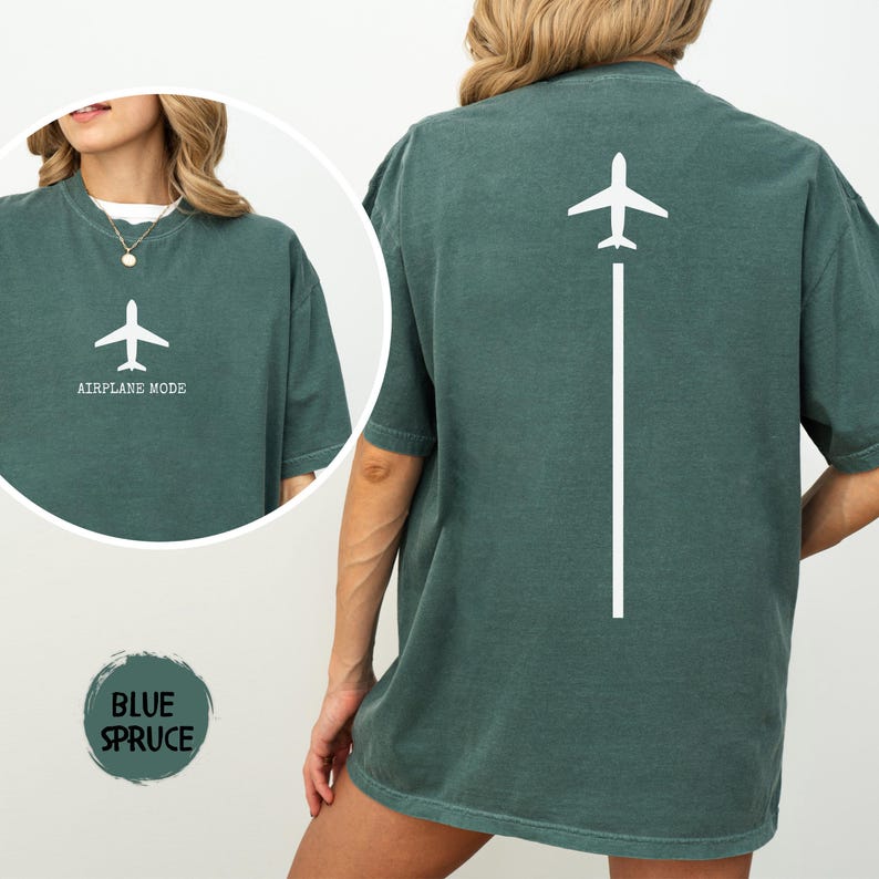 May include: A teal-colored t-shirt with a white airplane graphic and the text "AIRPLANE MODE" on the front. The back of the shirt features a white airplane graphic with a vertical line. The shirt is a relaxed fit.
