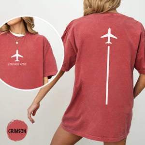 May include: Crimson-colored t-shirt with a white airplane graphic and the text "AIRPLANE MODE" on the front. The back of the shirt features a white airplane graphic with a vertical line. The shirt is a relaxed fit.