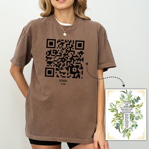 May include: A brown t-shirt with a black QR code and the text "JOHN 3:16". The QR code links to a Bible verse that reads "For God so loved the world that He gave His one and only Son, that whoever believes in Him shall not perish but have eternal life. John 3:16".