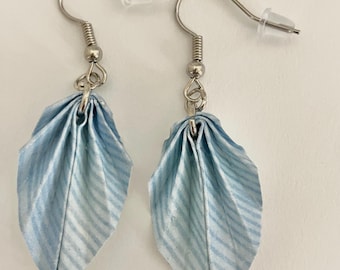 May include: A pair of dangle earrings featuring folded light blue and white striped paper leaf shapes. The earrings are attached to silver-toned metal fishhook wires with clear plastic backings, creating a lightweight and delicate appearance.