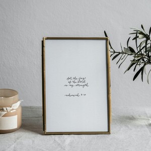 Może przedstawiać: Oprawiony wydruk z tekstem "feel the joy of the Lord is my strength" i mały szklany wazon z zielenią. Obecna jest również świeca w szklanym słoiku z drewnianą pokrywką i białą wstążką.