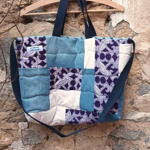 Peut inclure: Un sac cabas en patchwork bleu et blanc avec une bandoulière bleu marine. Le sac porte une étiquette indiquant "Un murmure sur la lune".