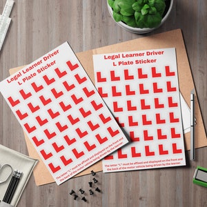 May include: Two white sheets with red 'L' plate stickers, text reads 'Legal Learner Driver L Plate Sticker'. The sheets are on a wooden surface with a pen, green plant, and other stationery items.