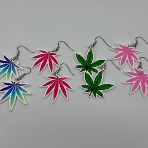 Könnte beinhalten: Eine Sammlung von Ohrringen in Blattform in verschiedenen Farben, darunter Grün, Rosa und Blau. Die Ohrringe bestehen aus glänzendem Material und haben silberfarbene Haken. Die Blätter sind weiß umrandet.