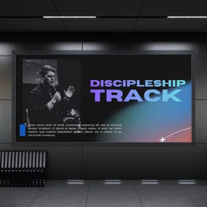 以下が含まれることがあります： 紫と青のグラデーションテキストで「DISCIPLESHIP TRACK」という言葉が表示された大きなデジタルディスプレイ。左側には、マイクに向かって話している男性の白黒画像があります。背景は暗いです。