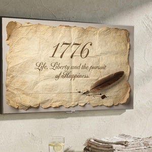 Peut inclure: Tableau encadré avec un papier parcheminé portant l'année "1776" et la citation "Life, Liberty and the pursuit of Happiness". Une plume et une tache d'encre sont également représentées. L'œuvre est au-dessus d'une table en bois.