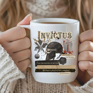 May include: White ceramic mug featuring the word "INVICTUS" in a decorative font, along with illustrations of a helmet, swords, and a shield. The mug also includes inspirational quotes and the phrase "UNCONQUERED".
