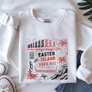 May include: A white crewneck sweatshirt featuring a graphic print with black and red ink. The design includes Moai statues, palm trees, a boat, sea turtles, and the text "EASTER ISLAND RAPA NUI" in the center. The garment has a Gildan brand label.