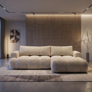 May include: A contemporary beige sectional sofa with an ottoman, set on a patterned rug. The sofa has a textured finish. The room features a wooden panelled wall and large windows with a city skyline visible in the background.