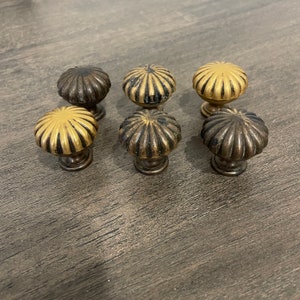 May include: Six decorative cabinet knobs with a scalloped design. The knobs are made of metal and have a gold and brown finish.