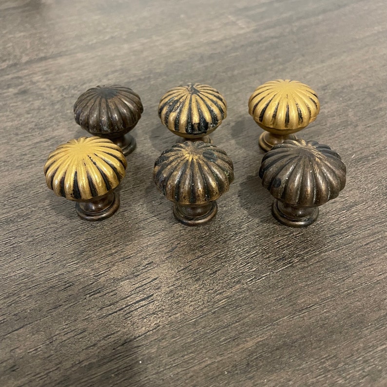 May include: Six decorative cabinet knobs with a scalloped design. The knobs are made of metal and have a gold and brown finish.