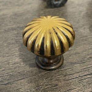 May include: A gold and black decorative knob with a scalloped design. The knob has a round top and a short, cylindrical base.