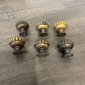 May include: Six antique-style cabinet knobs with a fluted design. The knobs are made of metal and have a brass finish. Some of the knobs have a darker patina.