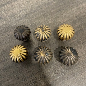 May include: Six decorative cabinet knobs with a fluted design. The knobs are made of metal and have a gold and black finish.