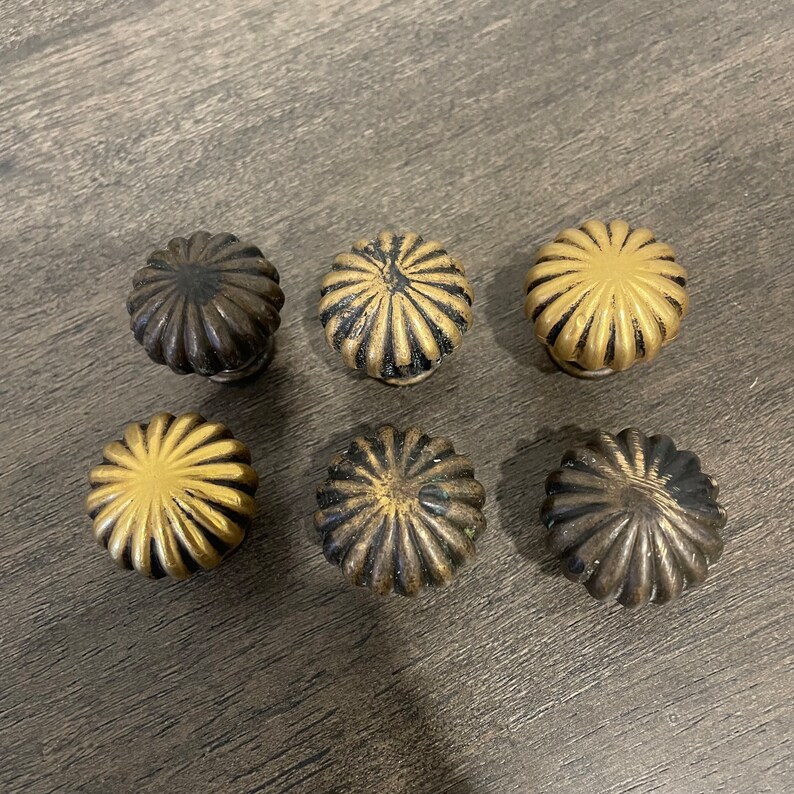 May include: Six decorative cabinet knobs with a fluted design. The knobs are made of metal and have a gold and black finish.