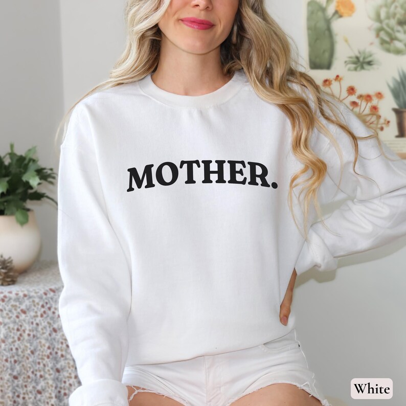 Womans white colored sweatshirt with black text that says Mother in arched text across the upper chest