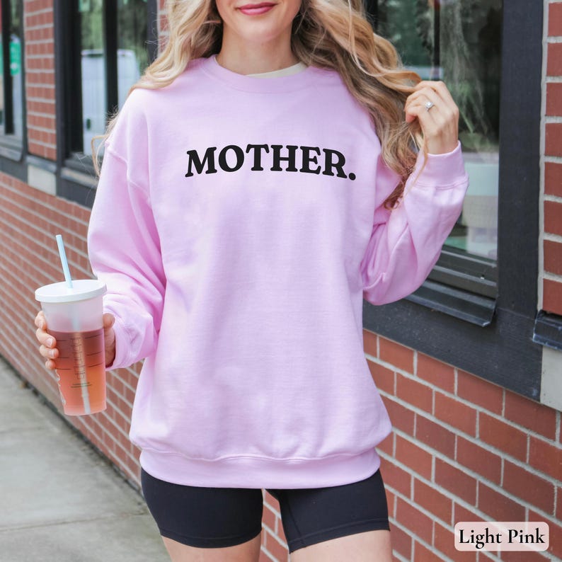 Womans light pink colored sweatshirt with black text that says Mother in arched text across the upper chest