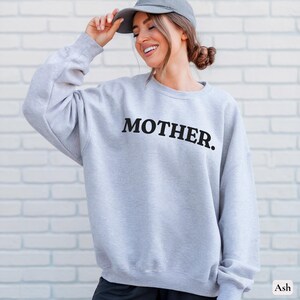 Womans ash colored sweatshirt with black text that says Mother in arched text across the upper chest