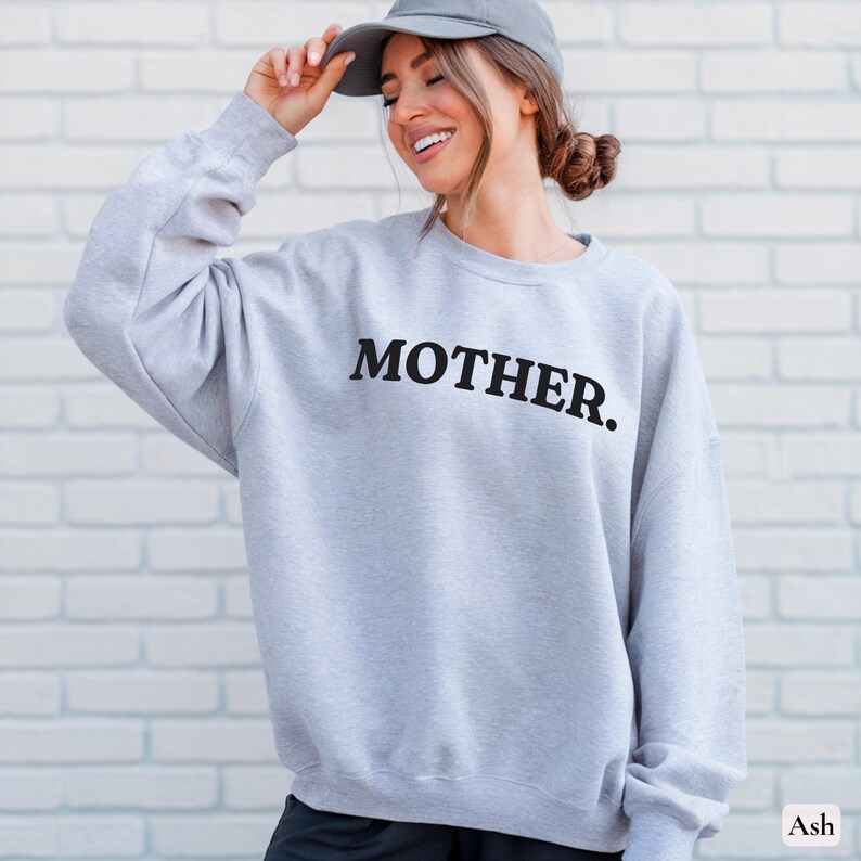 Womans ash colored sweatshirt with black text that says Mother in arched text across the upper chest