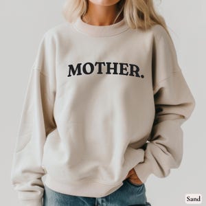 Womans sand colored sweatshirt with black text that says Mother in arched text across the upper chest