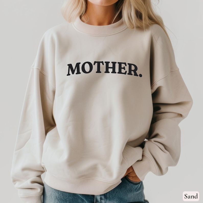 Womans sand colored sweatshirt with black text that says Mother in arched text across the upper chest