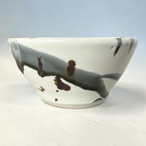 May include: A ceramic bowl with a white base featuring abstract, sweeping brushstrokes in dark gray and charcoal. The design includes scattered brown speckles and spots across the exterior surface, creating a textured, hand-crafted appearance.