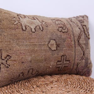 Puede incluir: Una almohada rectangular con un patr&oacute;n tejido marr&oacute;n y beige. La almohada tiene un dise&ntilde;o geom&eacute;trico con una cruz en el centro.