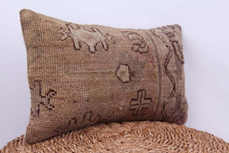 Puede incluir: Una almohada rectangular con un patr&oacute;n tejido marr&oacute;n y beige. La almohada tiene un dise&ntilde;o geom&eacute;trico con una cruz en el centro.