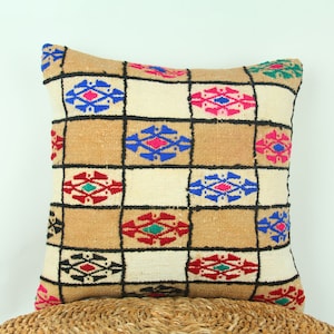 以下が含まれることがあります： 茶色、白、青、赤、緑、黒の幾何学模様が施された装飾的なクッション。クッションは織物で作られており、正方形の形をしています。