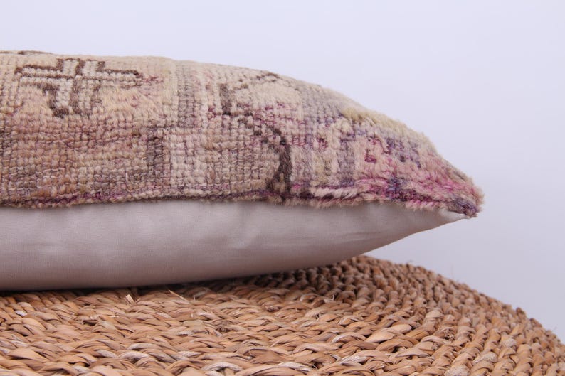 Puede incluir: Una almohada decorativa con una funda de tela estampada en beige, rosa y marr&oacute;n. La almohada tiene un respaldo blanco de algod&oacute;n y est&aacute; sentada sobre una superficie de mimbre tejido.