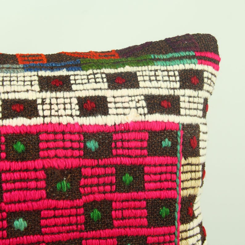 May include: A rectangular pillow with a brown, pink, white, and green geometric pattern. The pillow is made of woven fabric and has a fringed edge.