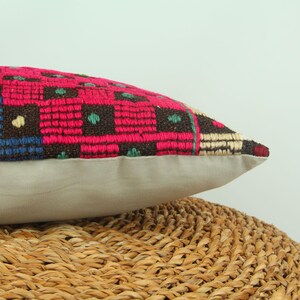 May include: A pink, brown, blue, and green patterned throw pillow with a beige backing. The pillow is sitting on a woven wicker surface.