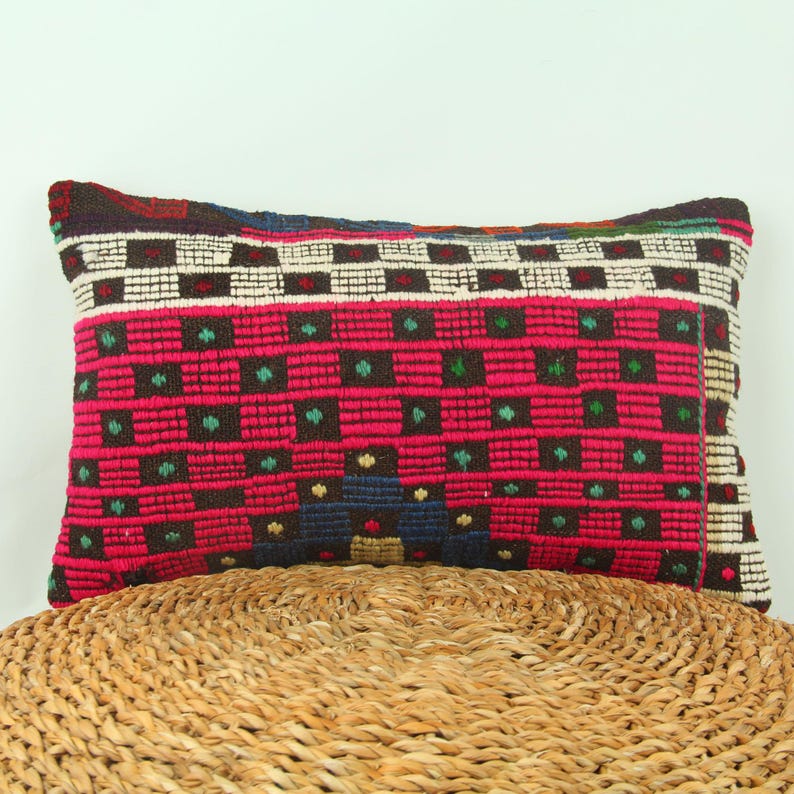 May include: A rectangular pillow with a colorful geometric pattern. The pillow is made of woven fabric and has a brown, pink, green, white, and blue design.